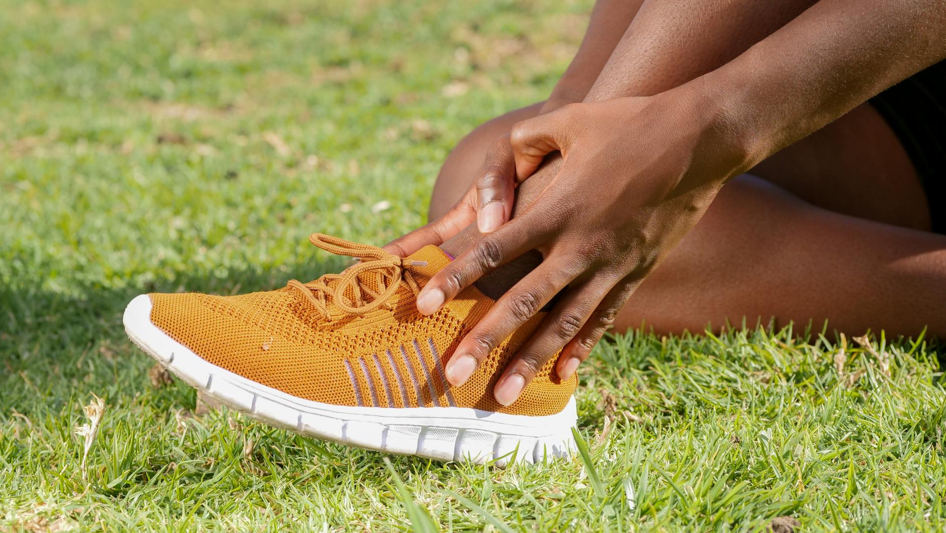 Biegacz trzyma bolącą kostkę w pomarańczowym bucie sportowym
