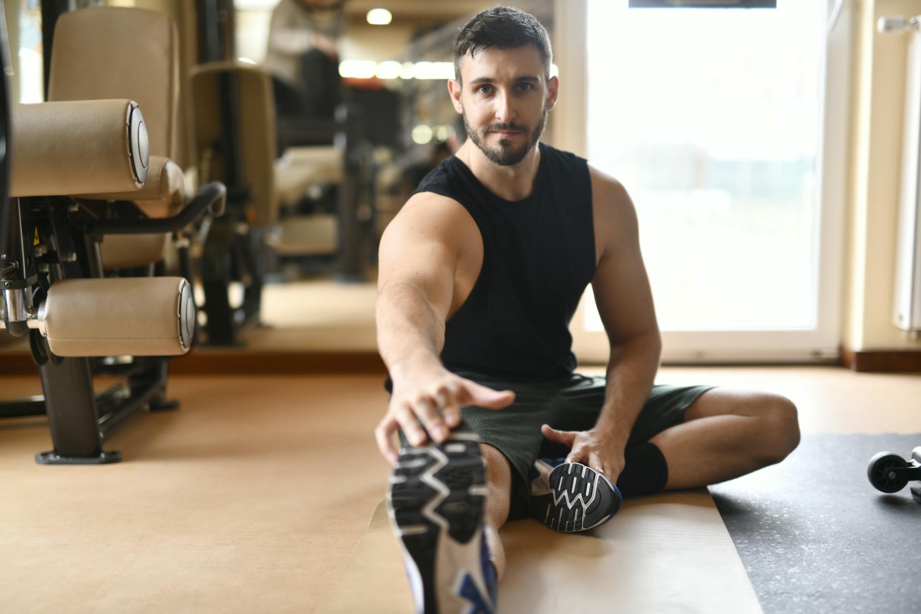 Mężczyzna w stroju sportowym rozciąga się na podłodze siłowni