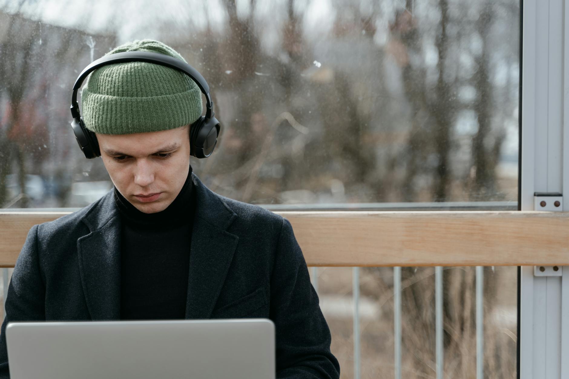 Jak wybrać idealną muzykę relaksacyjną do pracy, nauki i medytacji Mężczyzna w zielonej czapce słucha muzyki w słuchawkach, pracując na laptopie