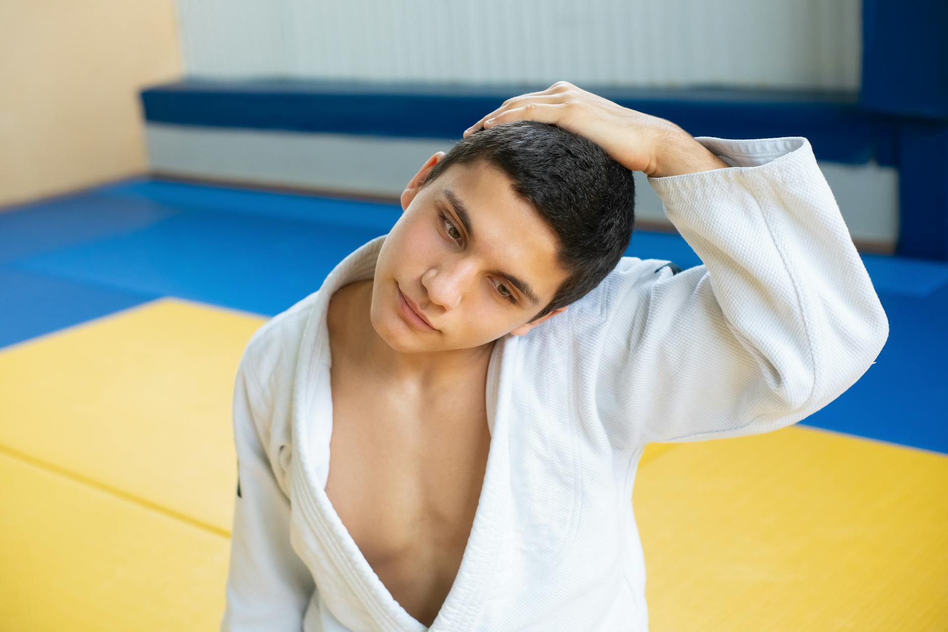 Mężczyzna w kimonie judo rozciąga kark w kolorowej sali treningowej