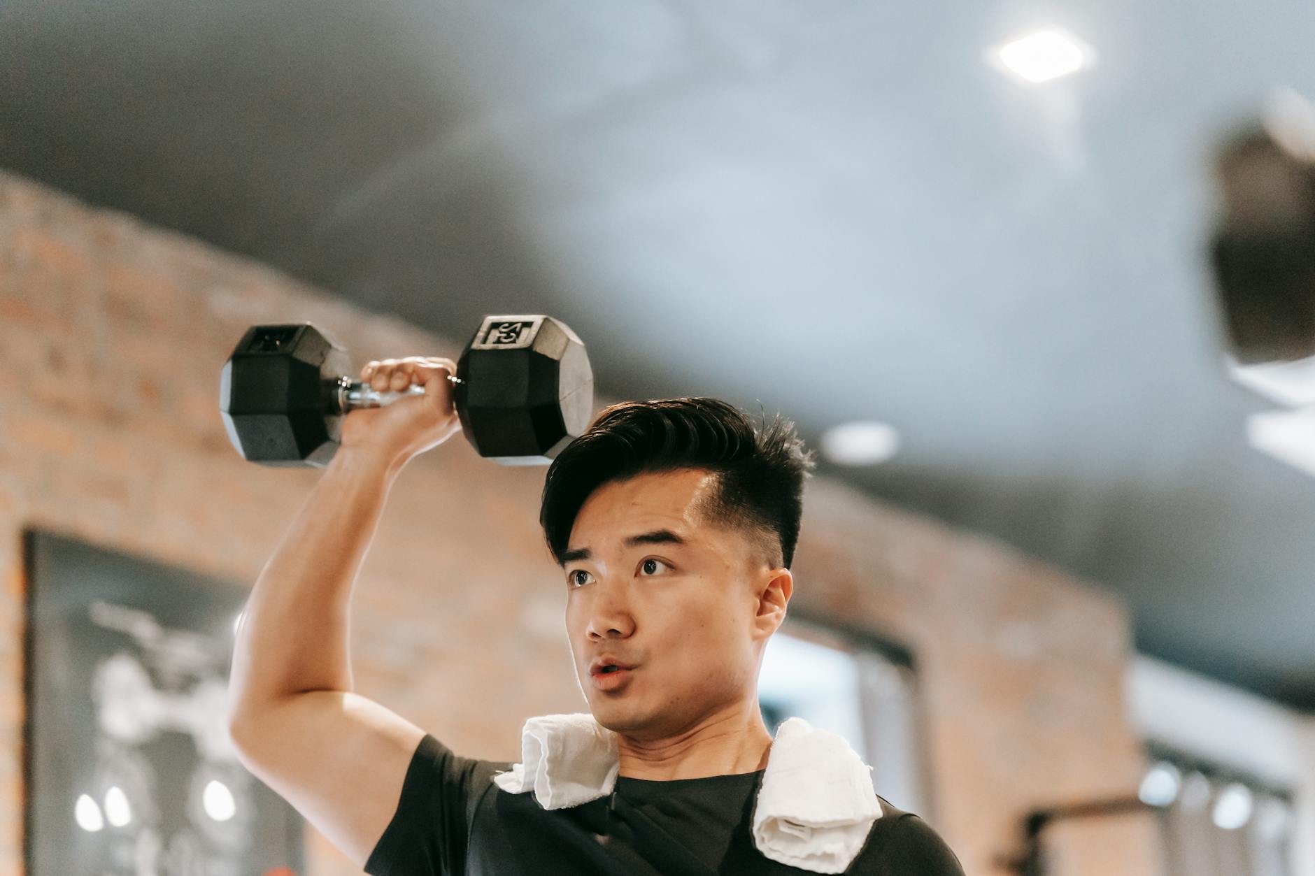 Mężczyzna ćwiczący barki i biceps z ciężkim hantlem na siłowni