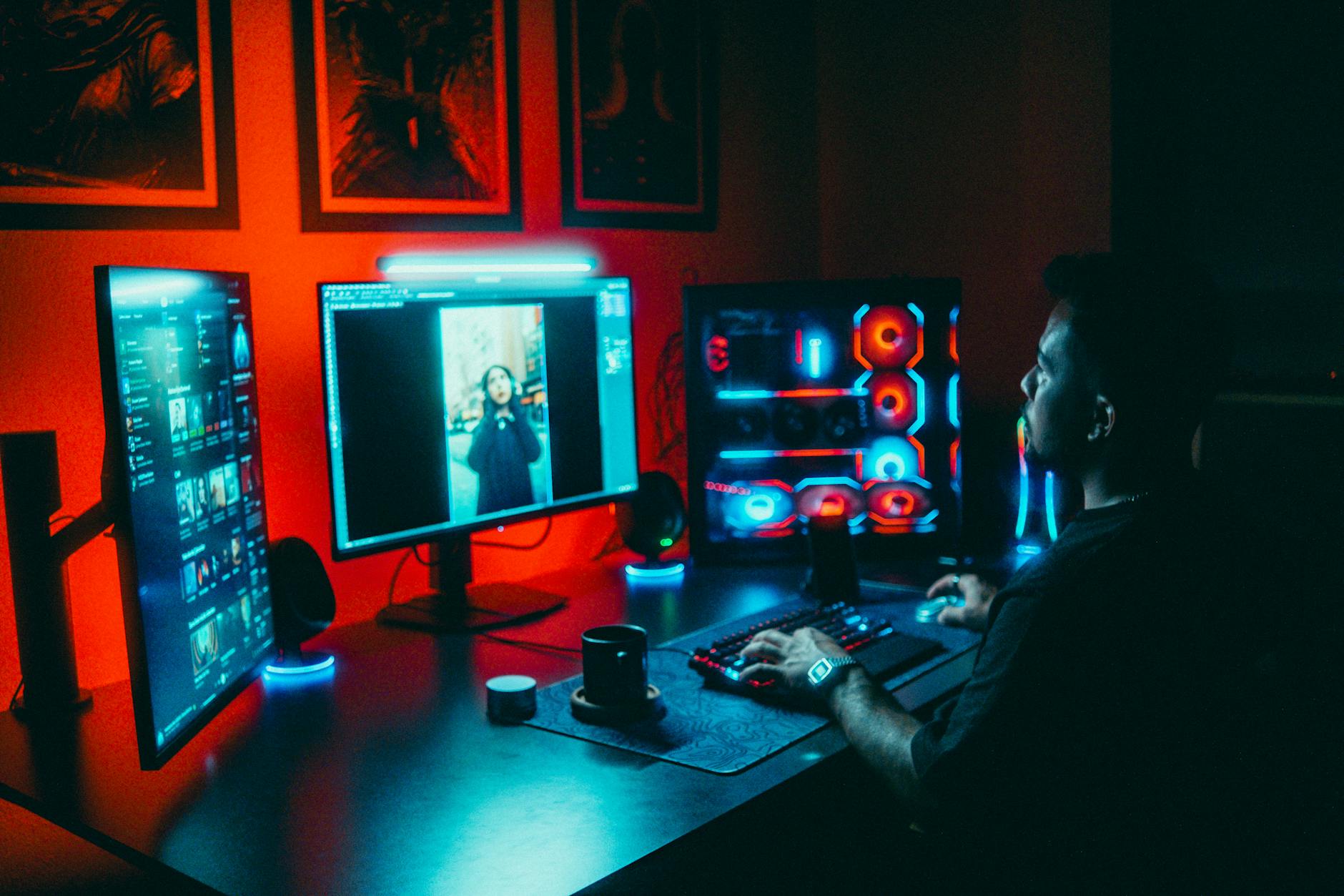 Młody mężczyzna tworzy grę przy kilku monitorach w neonowym pokoju