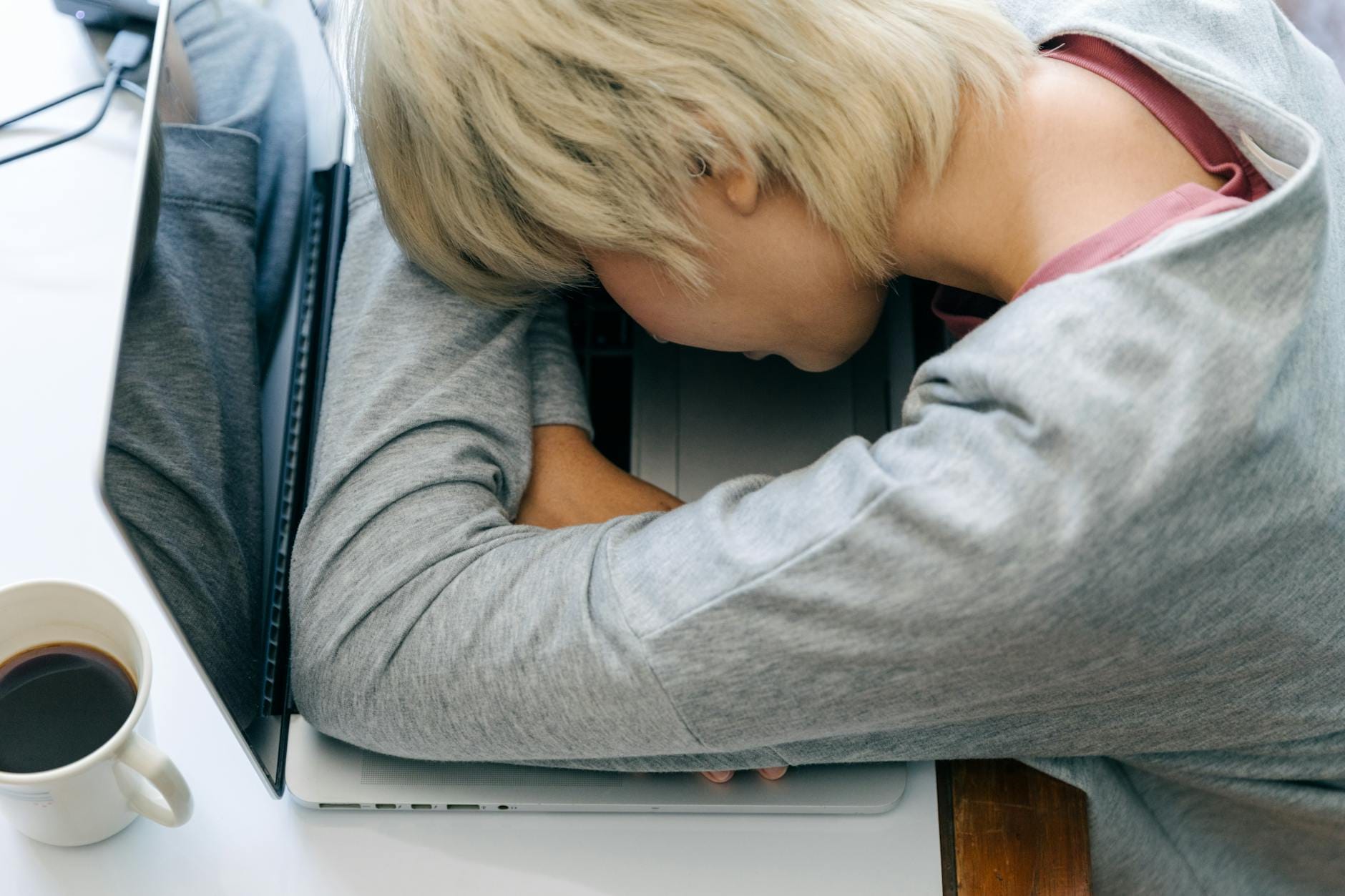 Zmęczona kobieta śpi przy laptopie z kubkiem kawy po długiej pracy