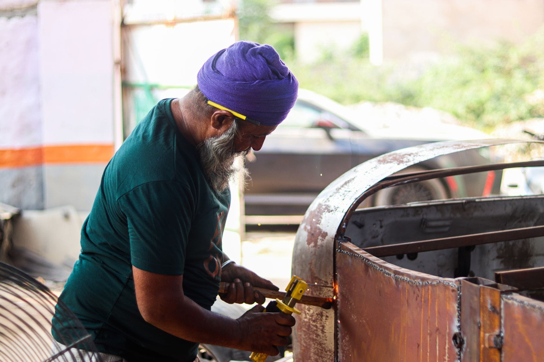 Starszy mężczyzna w turbanie naprawia metalowy element na zewnątrz