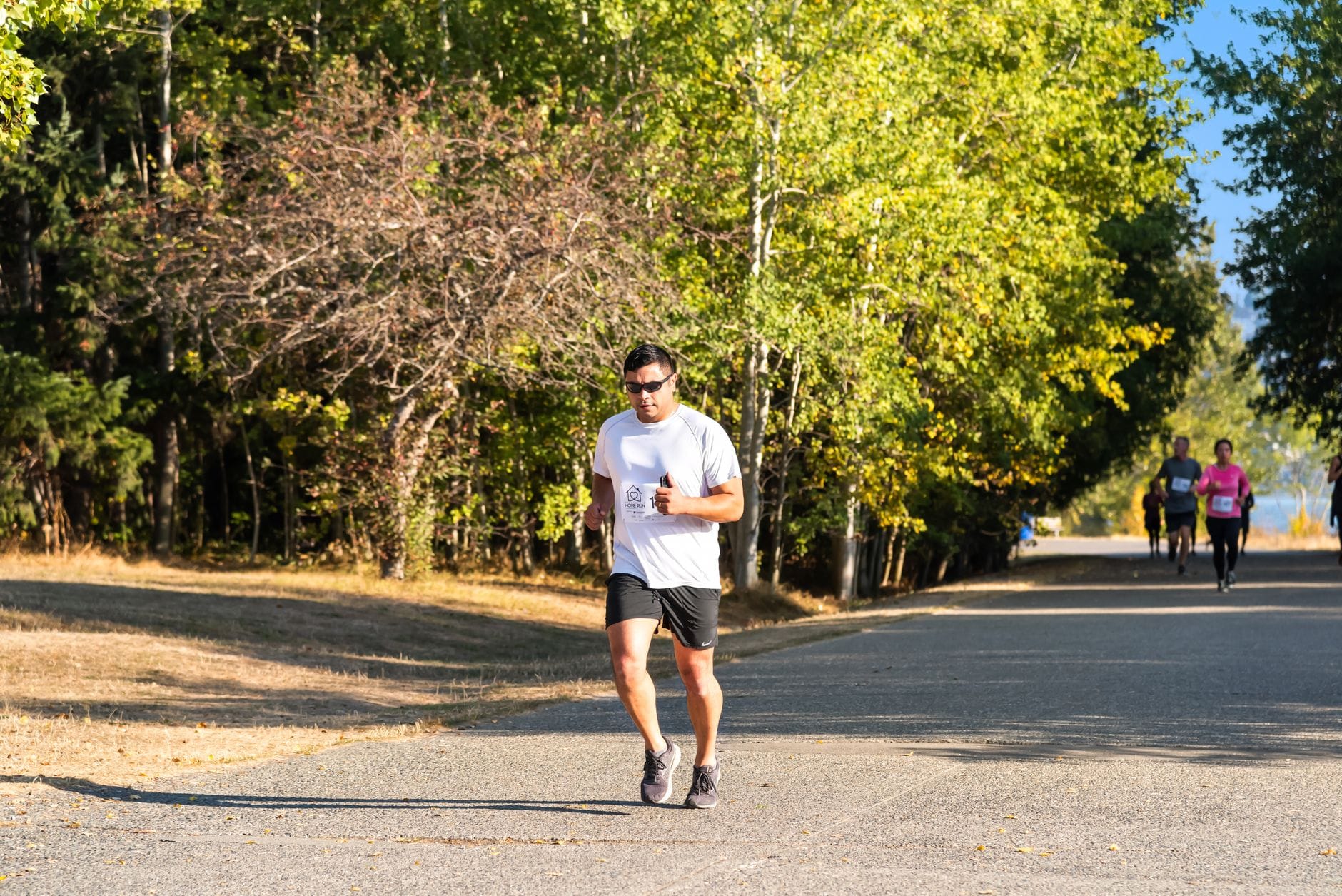 Biegacze maratonu na słonecznej, zadrzewionej alejce