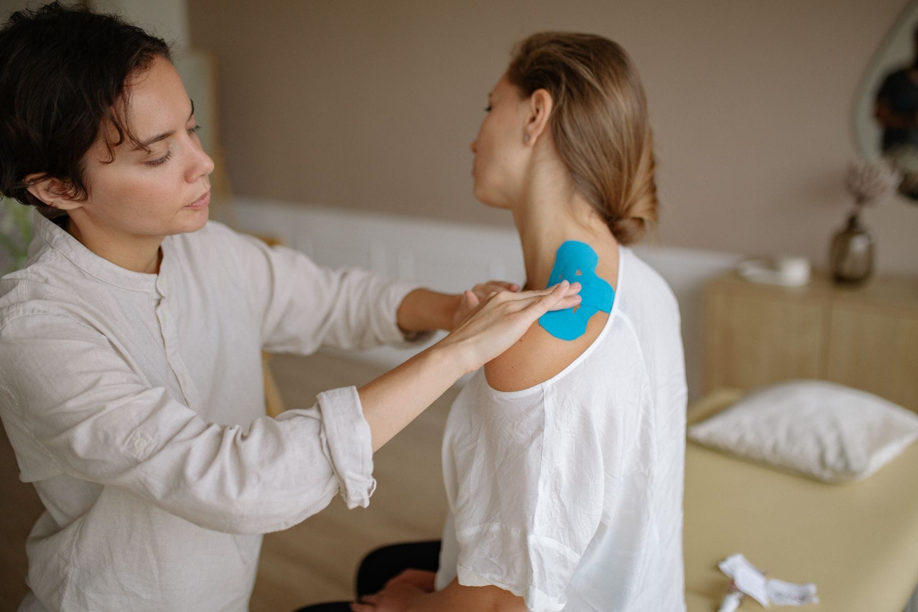 Fizjoterapeuta nakleja niebieskie tejpy na bolący bark pacjenta