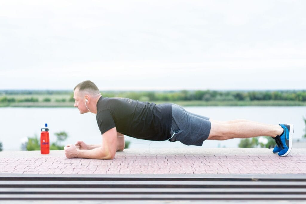 Mężczyzna w stroju sportowym wykonuje plank nad jeziorem ze słuchawkami